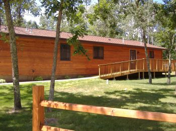 Outside View of Cabin #19 with large deck, BBQ grill and picnic table.  The deck faces North; parking is at the south of this cabin.  The Ramp shown in this picture leads to the kitchen entry door and the spacious deck.